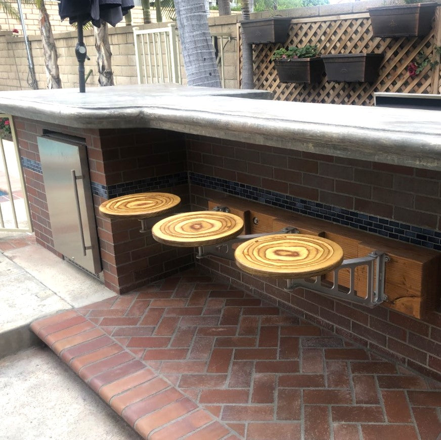 A set of four custom bar stools with adjustable wooden seats, mounted on a brick wall with a steel backplate, in an outdoor setting.