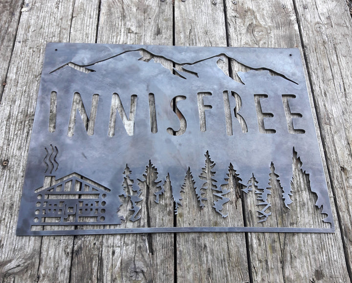 This sign is displays a mountain range in the background with a forest and cabin. The sign reads, "INNISFREE".