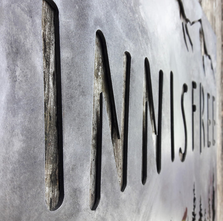 This sign is displays a mountain range in the background with a forest and cabin. The sign reads, "INNISFREE".