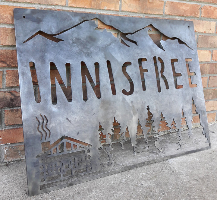 This sign is displays a mountain range in the background with a forest and cabin. The sign reads, "INNISFREE".