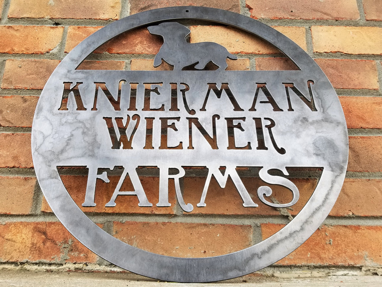 This is a custom round metal sign that features a wiener dog and reads from the top down, "Knierman Wiener Farms"