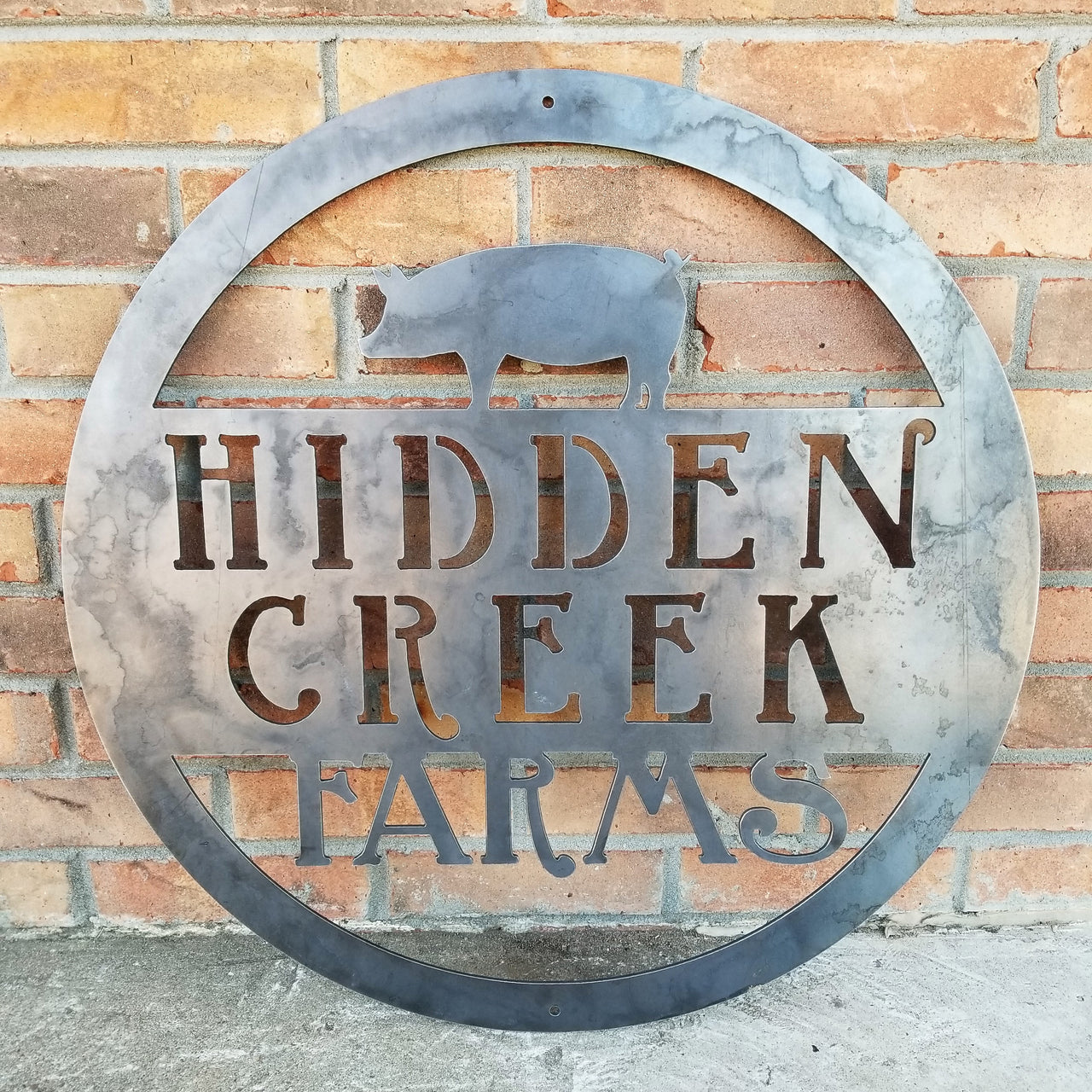 This is a custom round metal sign that features a Pig and reads from the top down, "Hidden Creek Farms"