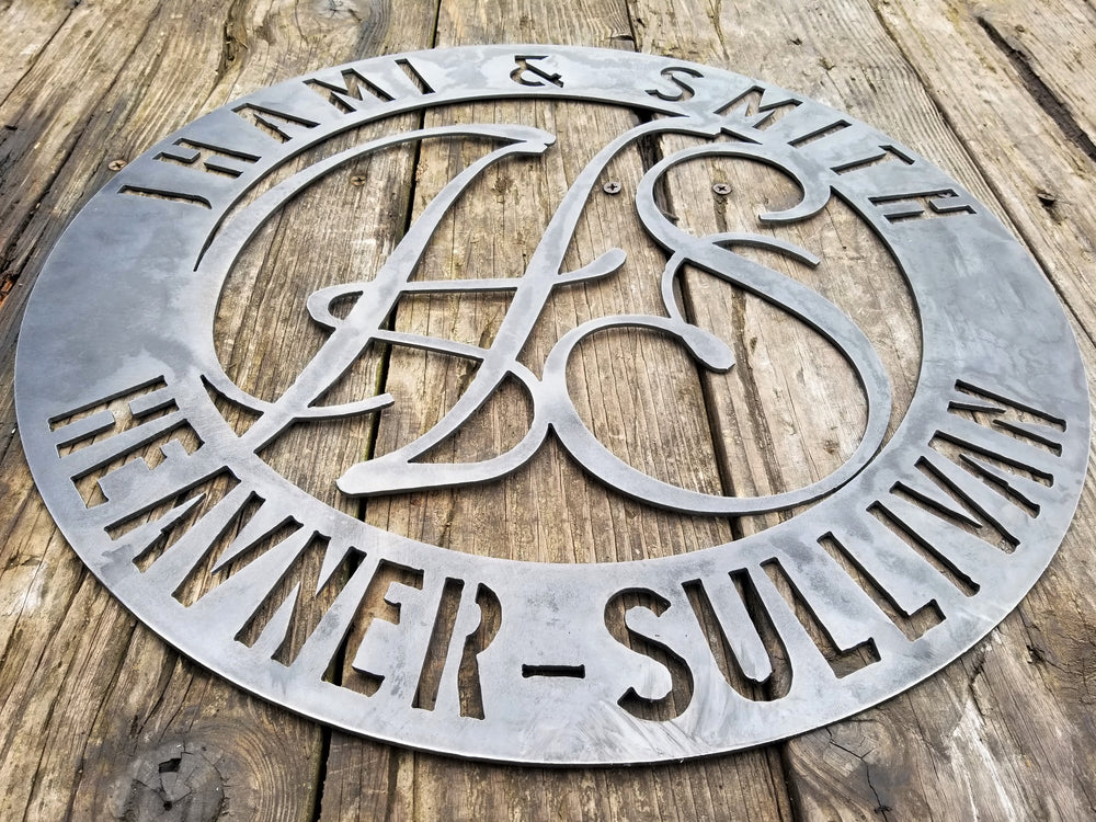 Round raw steel monogram with two lines of text and two letters in the center. The sign reads, " Jhami & Smith, Heavner-Sullivan"