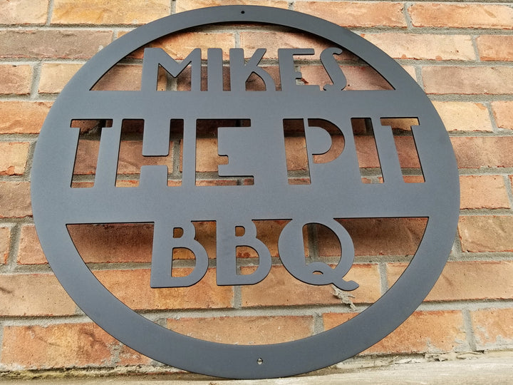 This is a round art deco. sign that has three lines of text. The sign reads, " Mikes The Pit BBQ"