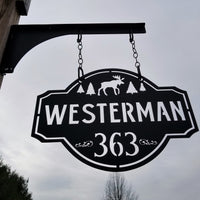 Thumbnail for This is a personalized metal address sign that hangs from a hanging bracket mounted to a wooden post.  The sign is powder coated black and features a forest scene with a moose in the center. The sign reads, 