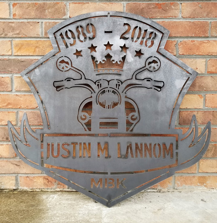 This is a memorial sign with an established year, dipicting an image of a motorcylce.  The bottom has a name and reads, "Justin M. Lannom".