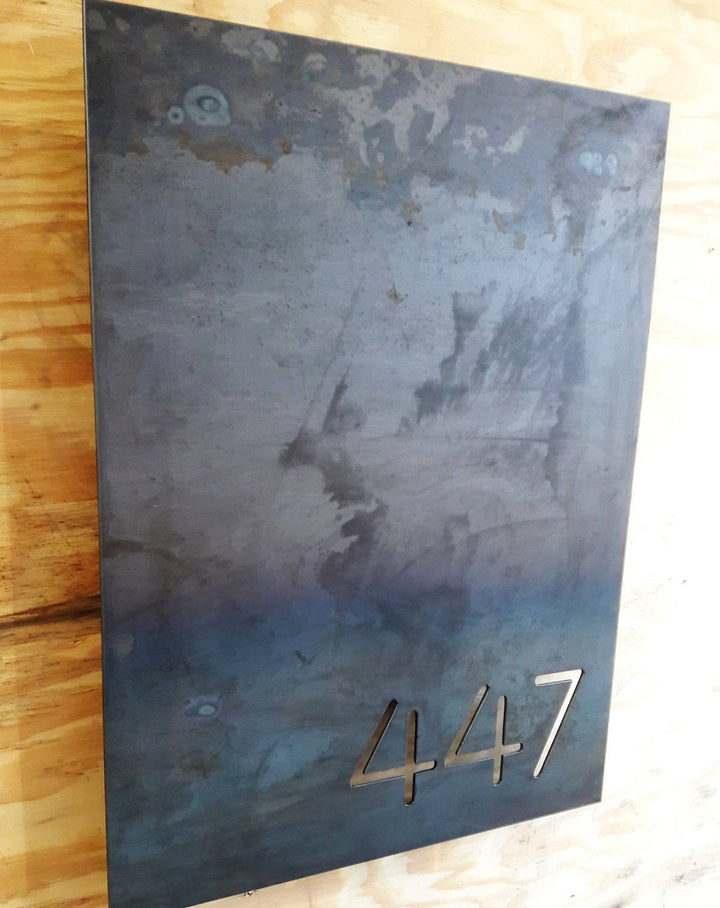 This is a personalized metal sign that has brackets welded to the back of the sign so that it stands one inch off the wall. It is a modern address sign in the shape of a rectangle and reads, "447"