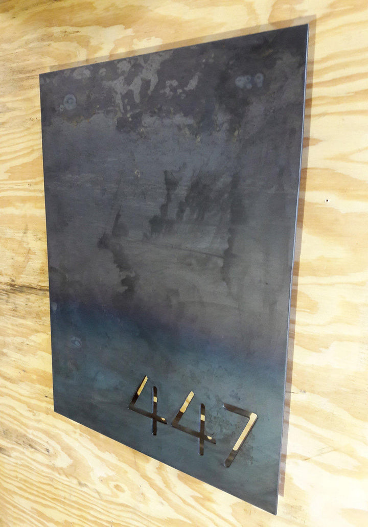 This is a personalized metal sign that has brackets welded to the back of the sign so that it stands one inch off the wall. It is a modern address sign in the shape of a rectangle and reads, "447"