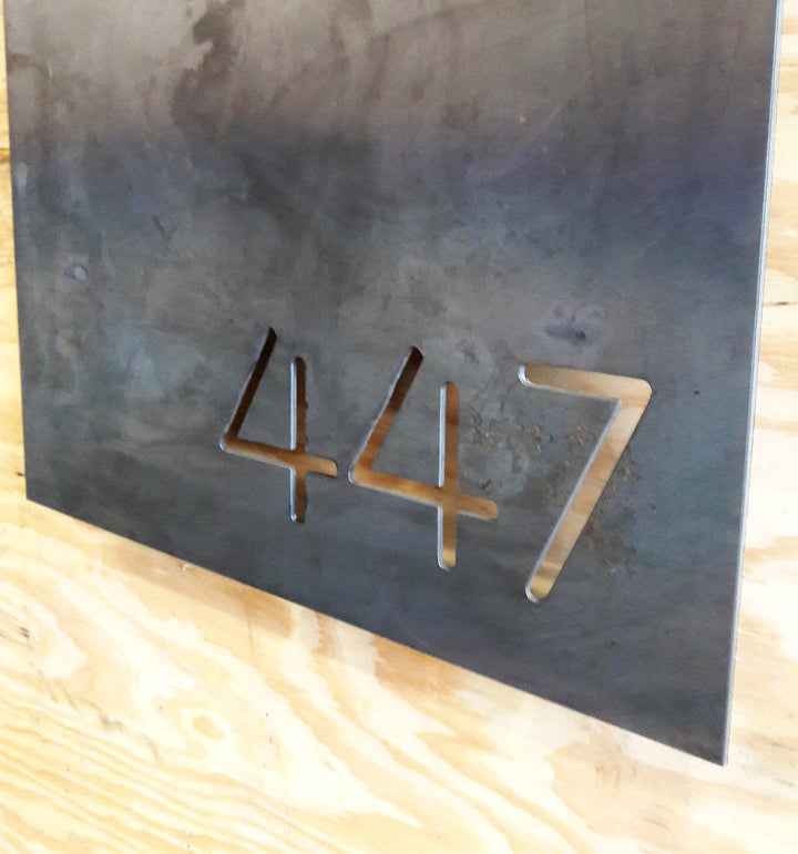 This is a personalized metal sign that has brackets welded to the back of the sign so that it stands one inch off the wall. It is a modern address sign in the shape of a rectangle and reads, "447"