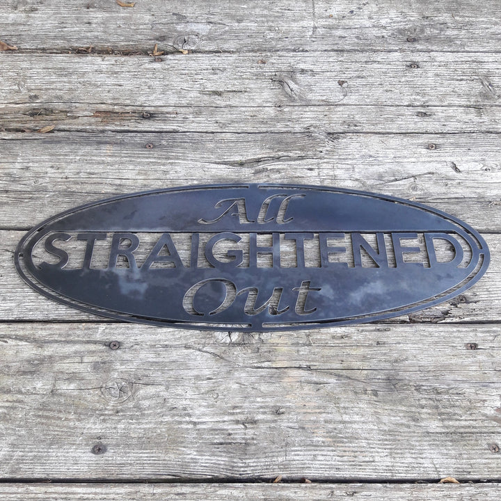 This metal sign is an oval, it has three lines of text. The sign reads, "All Straightened Out"