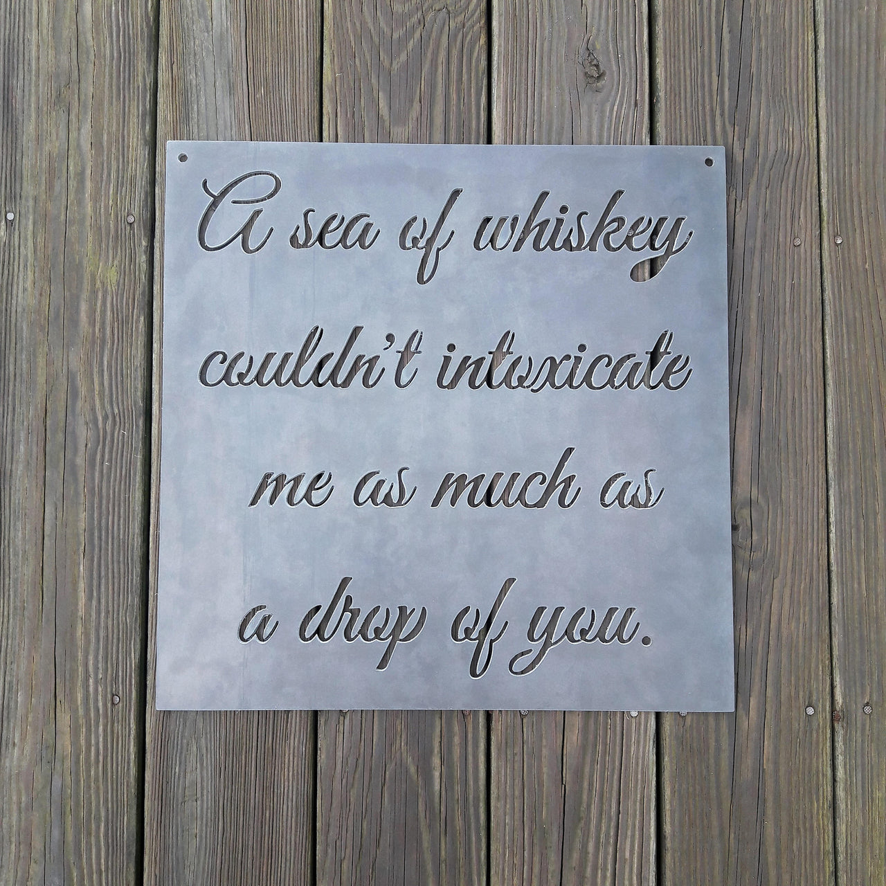 Square plaque with cursive writing in it. The sign reads, " A sea of whiskey couldn't intoxicate me as much as a drop of you."