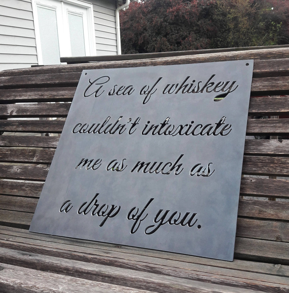 Square plaque with cursive writing in it. The sign reads, " A sea of whiskey couldn't intoxicate me as much as a drop of you."