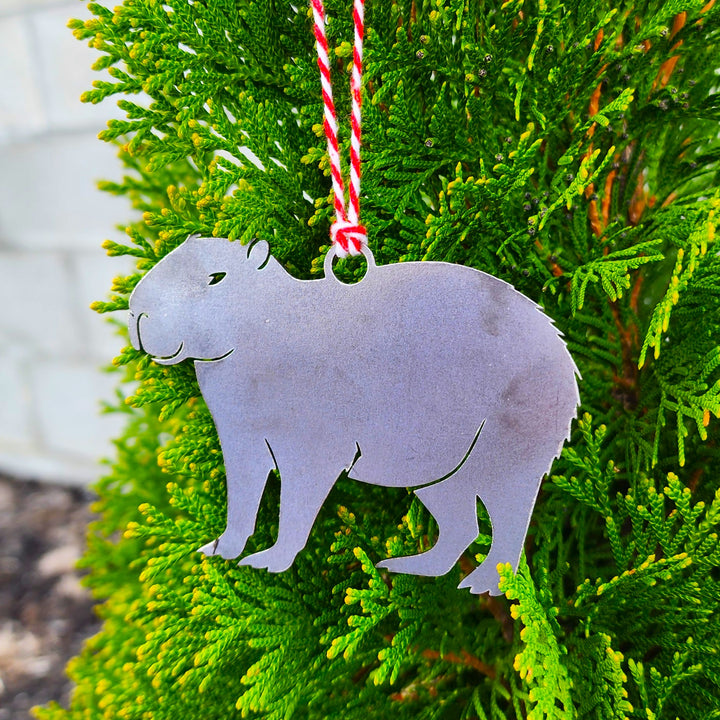 Metal capybara ornament hanging on a Christmas tree