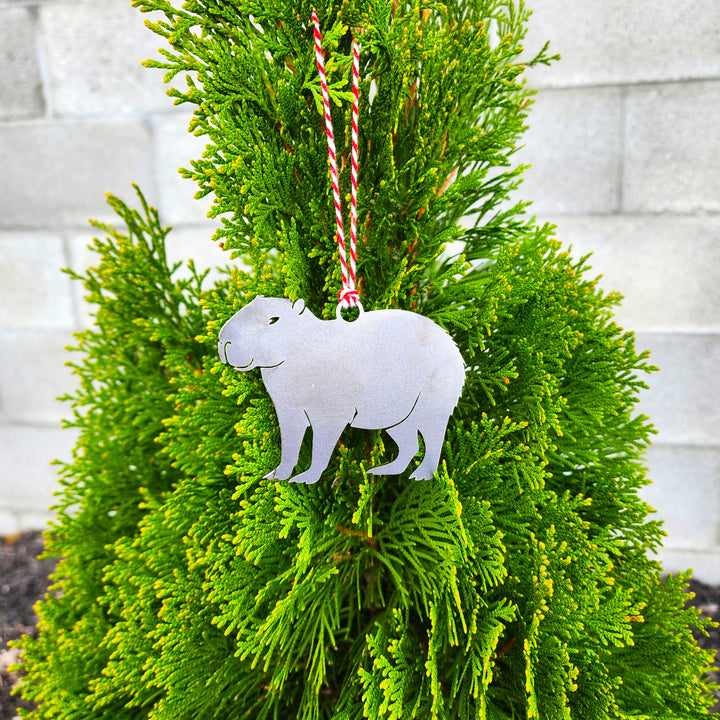 Metallic capybara ornament hanging on a green bush with a white wall background