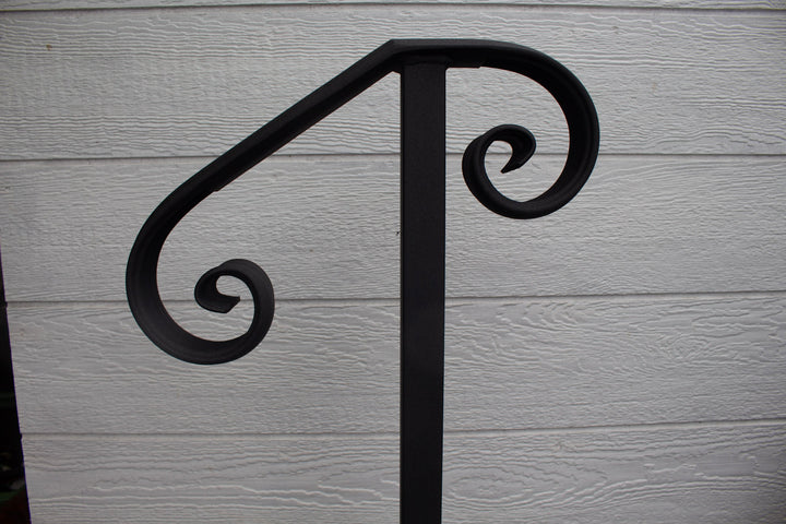 A close-up image of a black metal one step handrail with a textured flat finish, showing the handle's design and the mounting bracket against a wooden background.