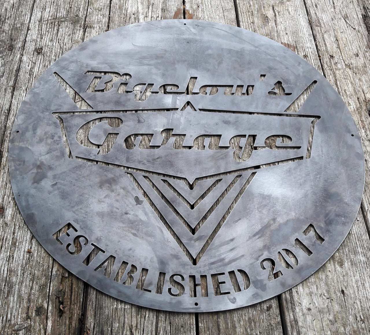 This is a rustic round metal garage sign which reads, "Bigelow's Garage, Established 2017"