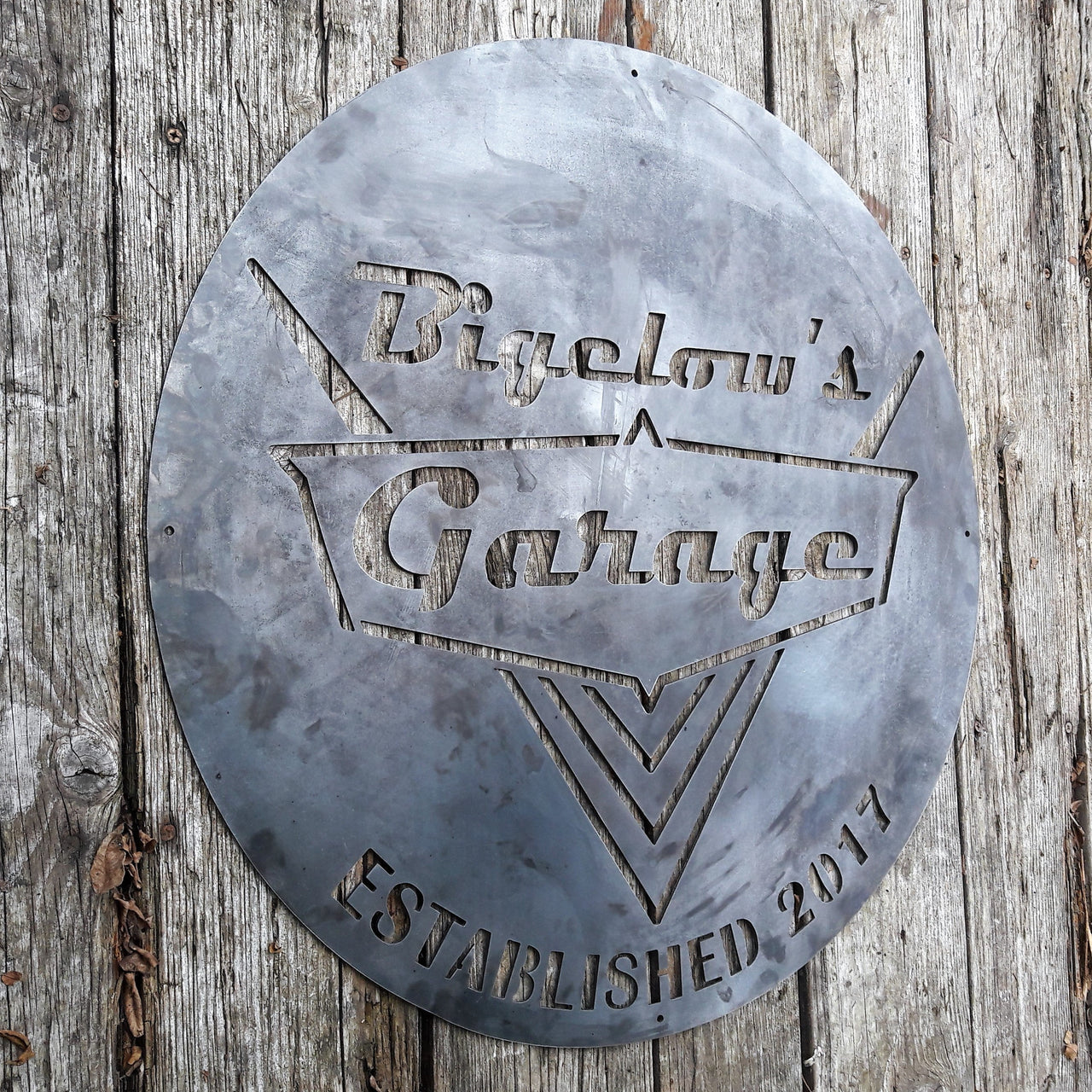 This is a rustic round metal garage sign which reads, "Bigelow's Garage, Established 2017"