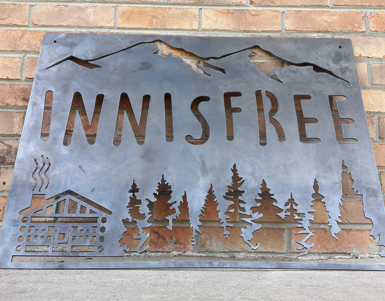 This sign is displays a mountain range in the background with a forest and cabin. The sign reads, "INNISFREE".