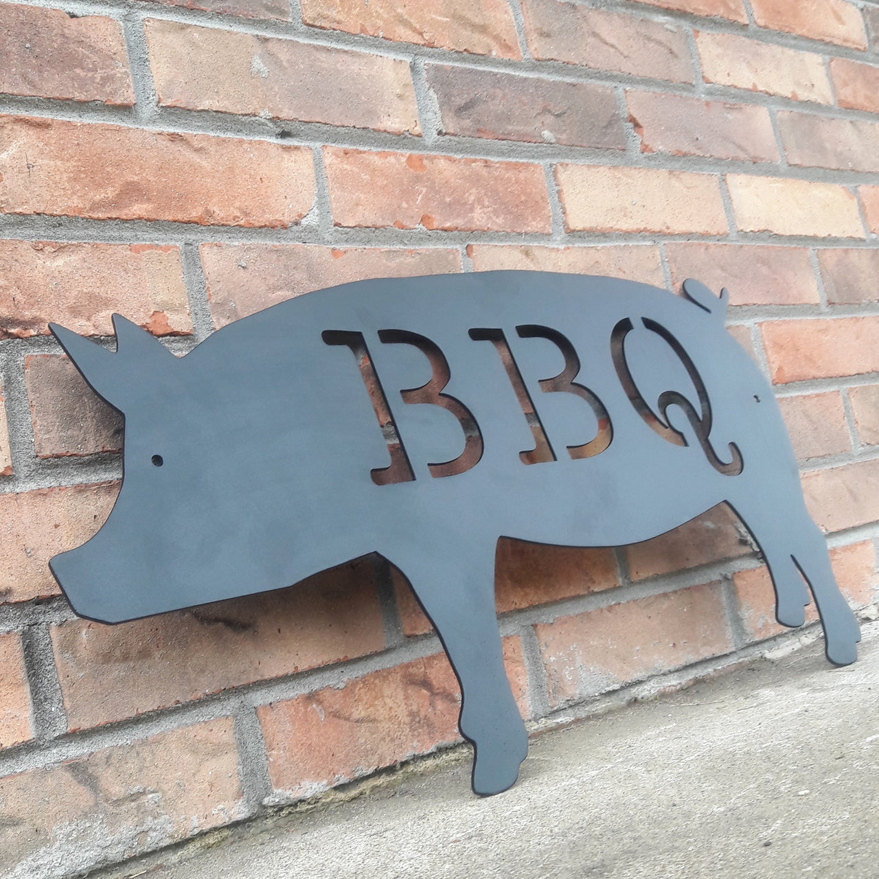 This is a black powder coated metal sign in the shape of pig with two 1/4" mounting holes. The sig reads, "BBQ"