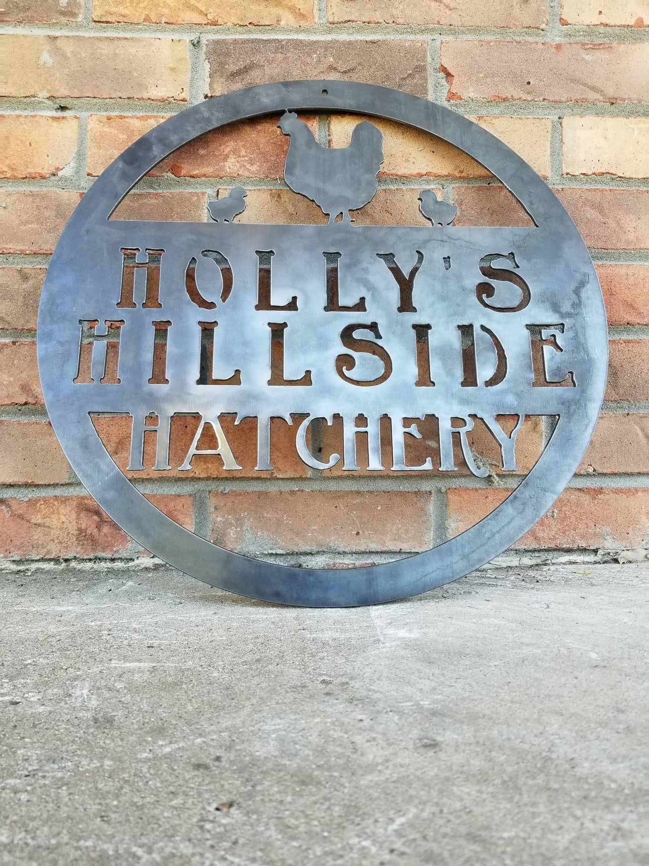 This metal sign is personalized and has the image of a chicken and two chicks at the top. The sign reads, "Holly's Hillside Hatchery".