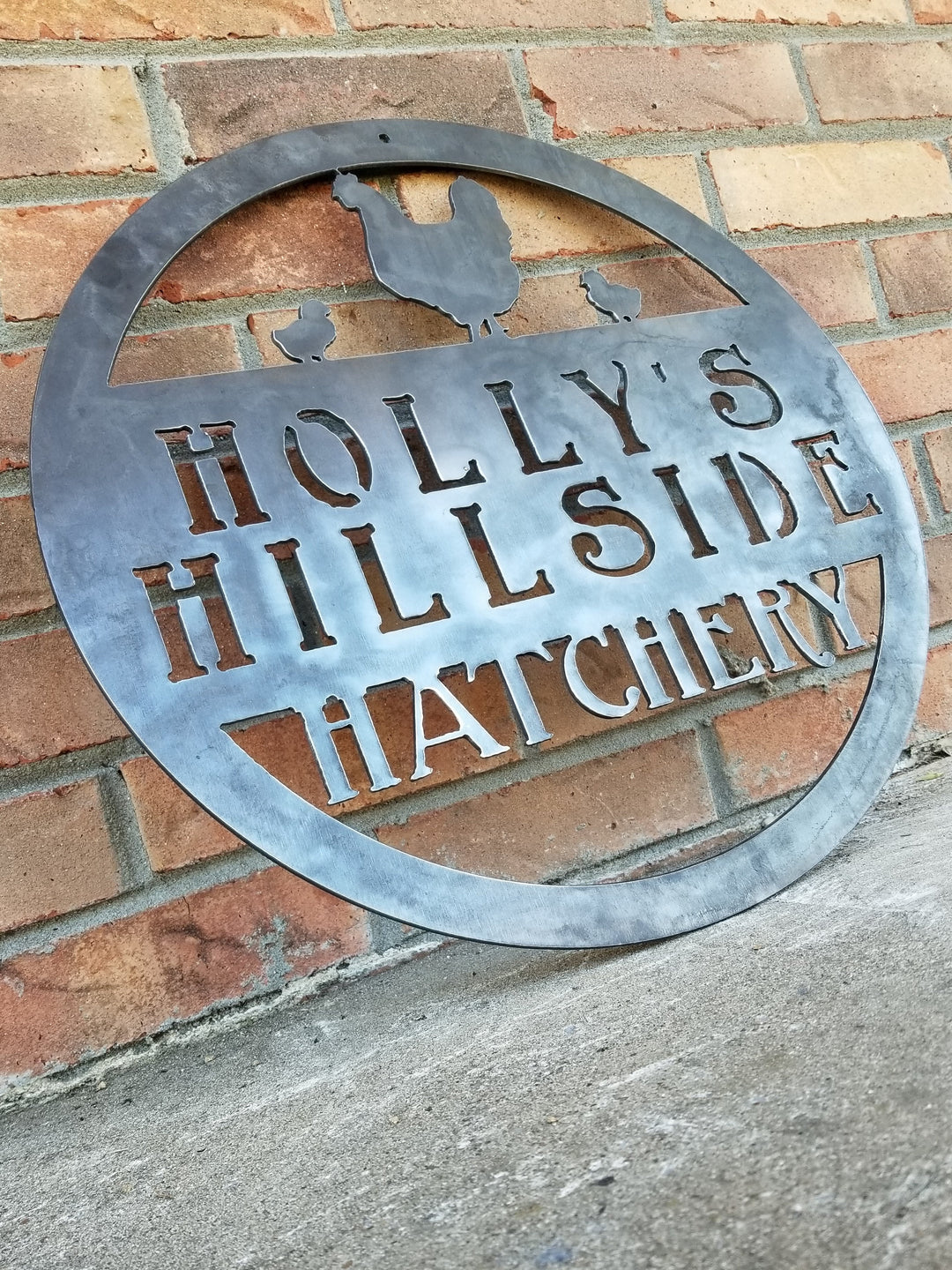 This metal sign is personalized and has the image of a chicken and two chicks at the top. The sign reads, "Holly's Hillside Hatchery".