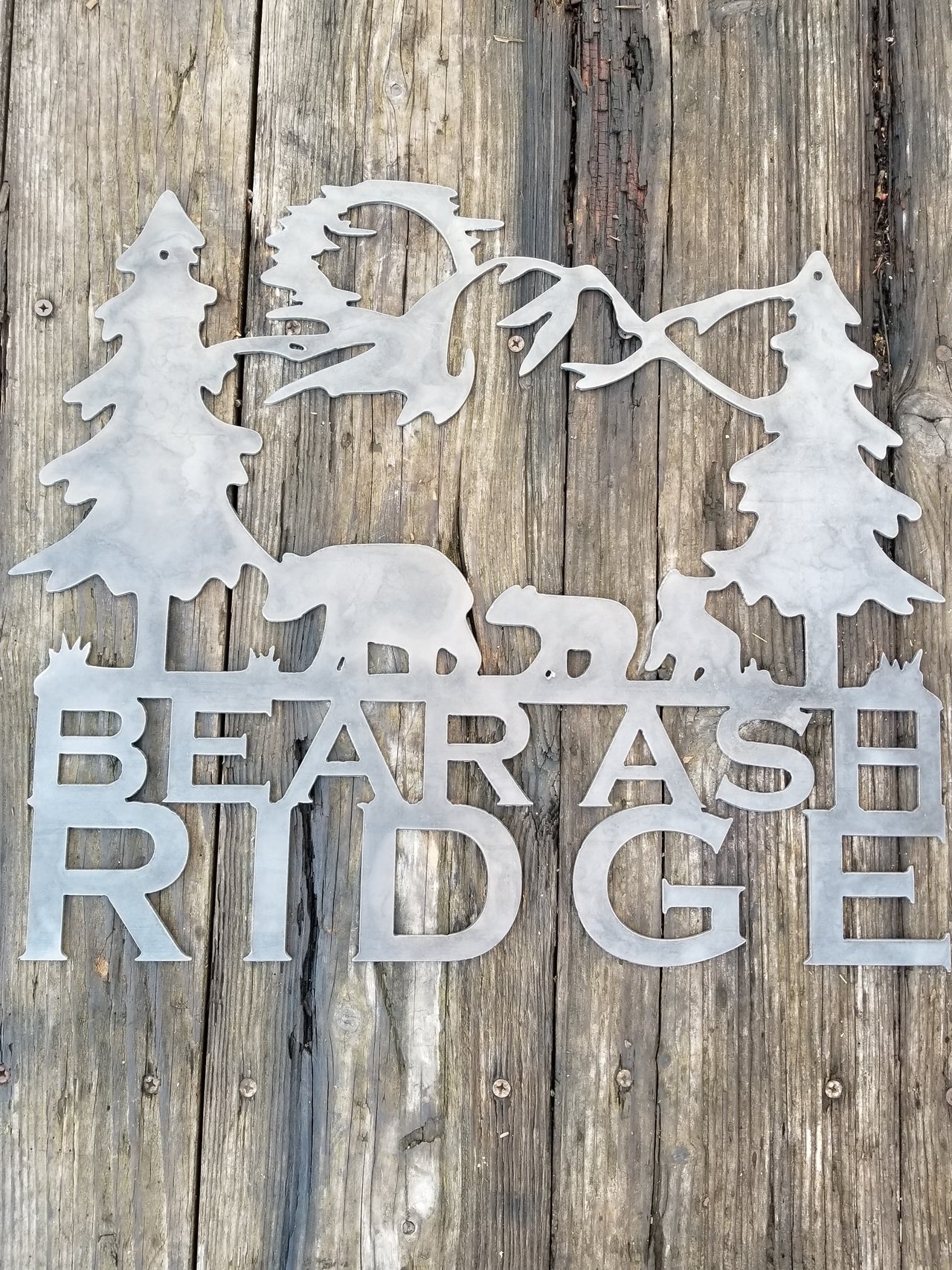 A tree scene with a family of bears and the sun in the background. Underneath the scene the metal sign reads, "Bear Ash Ridge"