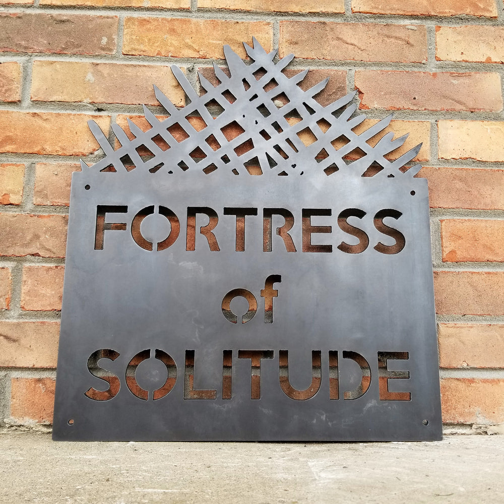 A metal man cave sign with a geometric pattern and the text 'FORTRESS OF SOLITUDE' displayed on it, set against a brick wall.