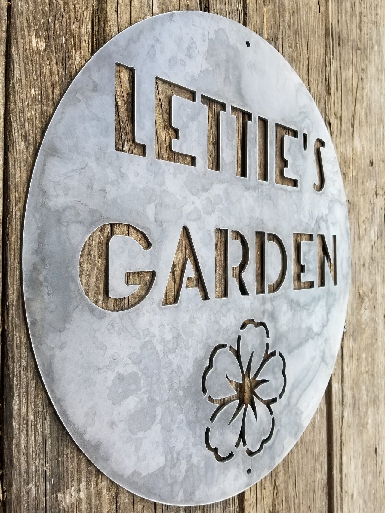 This is a round sign with an image of a flower below two lines of text which read, "Lettie's Garden".