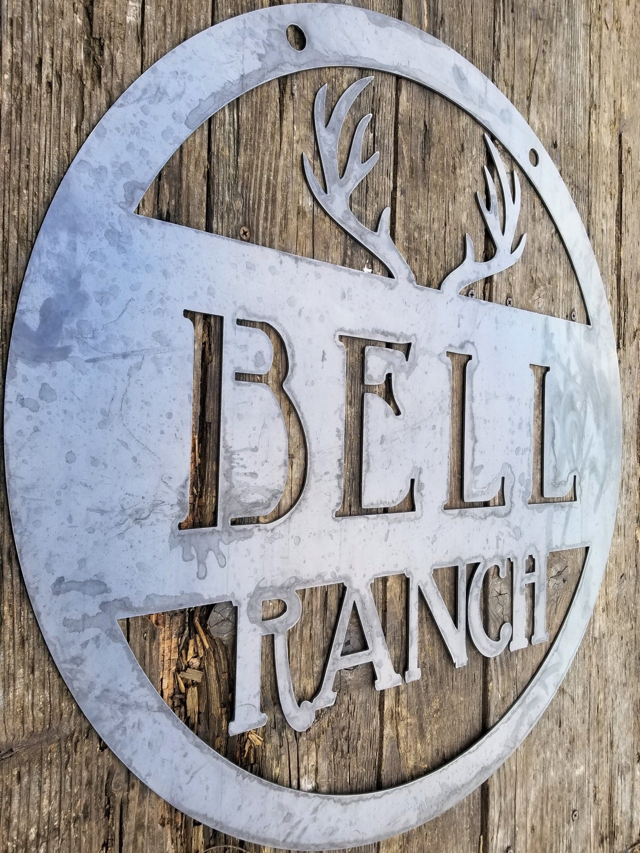 Round metal sign with an image of antlers at the top and two lines of text which read, "Bell Ranch"