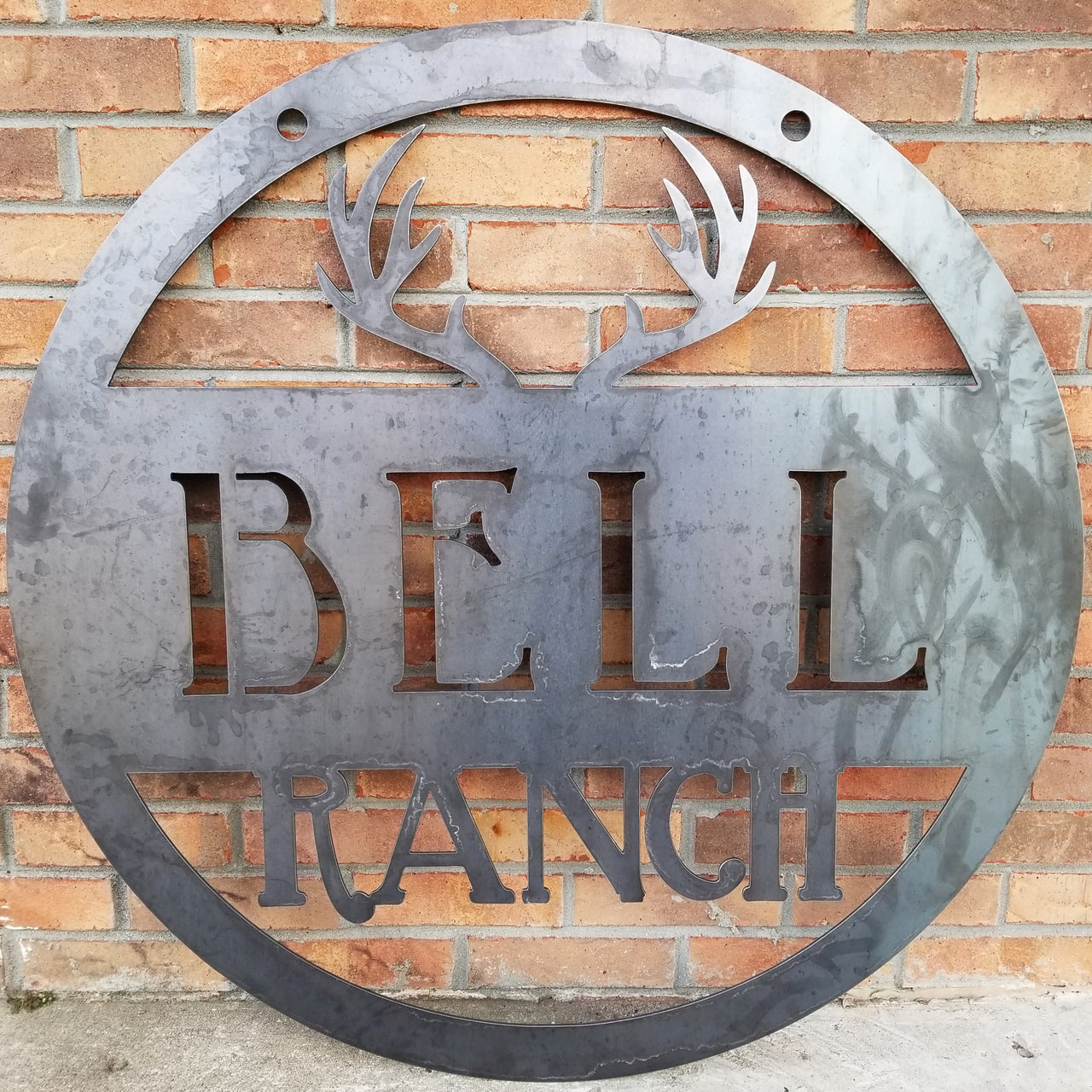 Round metal sign with an image of antlers at the top and two lines of text which read, "Bell Ranch"