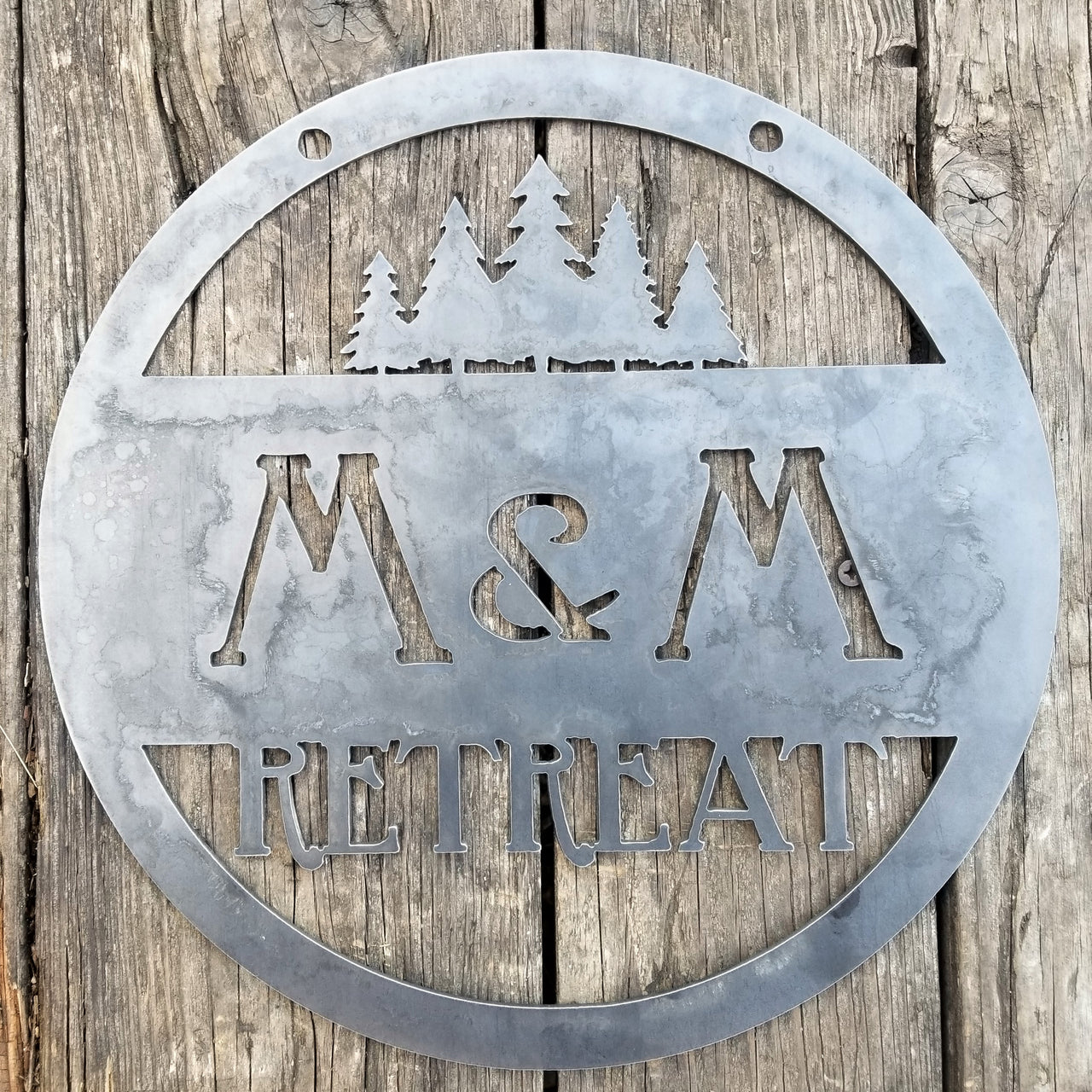 This custom metal sign has a cluster of trees at the top and reads, "M&M Retreat"