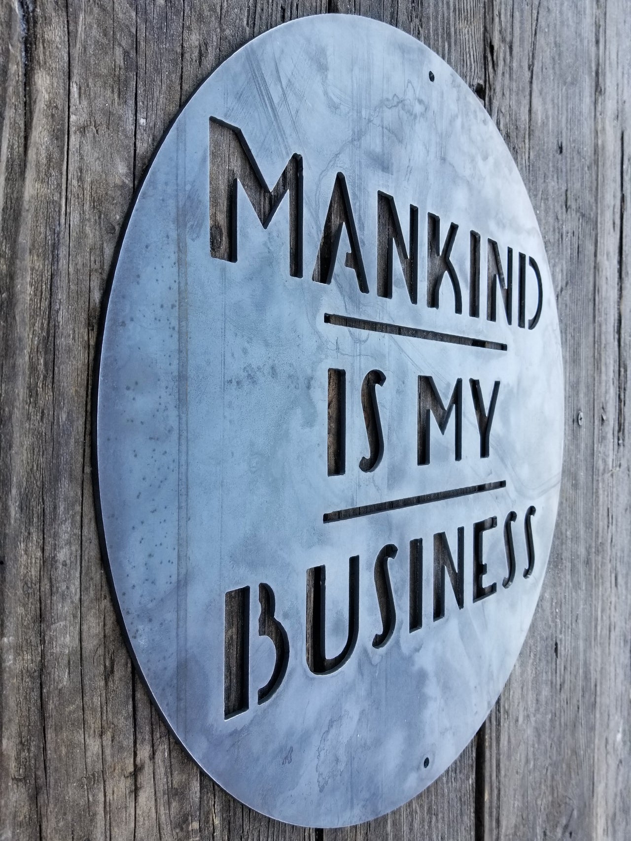 This is a round art deco sign that has three lines of text with a straight line seperating them. The sign reads, "Mankind Is My Business"