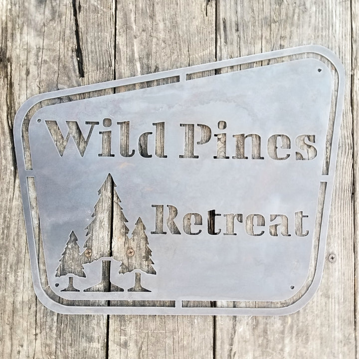 This sign has a vintage design and depicts a group of trees. It reads, "Wild Pines Retreat".