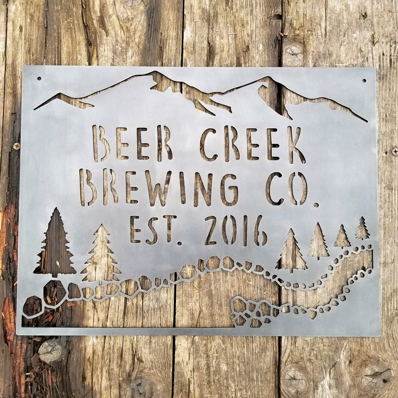 This sign showcases a mountain background with trees and a creek. The sign reads, " Beer Creek Brewing Co. Est. 2016".