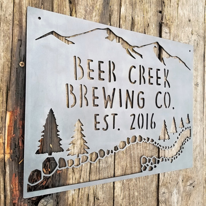 This sign showcases a mountain background with trees and a creek. The sign reads, " Beer Creek Brewing Co. Est. 2016".