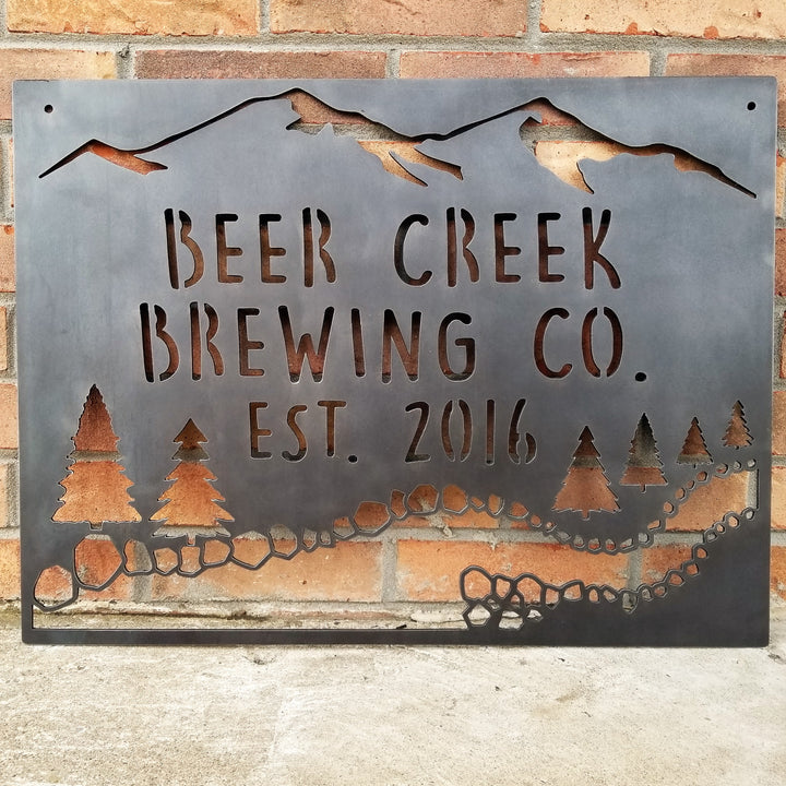 This sign showcases a mountain background with trees and a creek. The sign reads, " Beer Creek Brewing Co. Est. 2016".