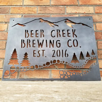 Thumbnail for This sign showcases a mountain background with trees and a creek. The sign reads, 