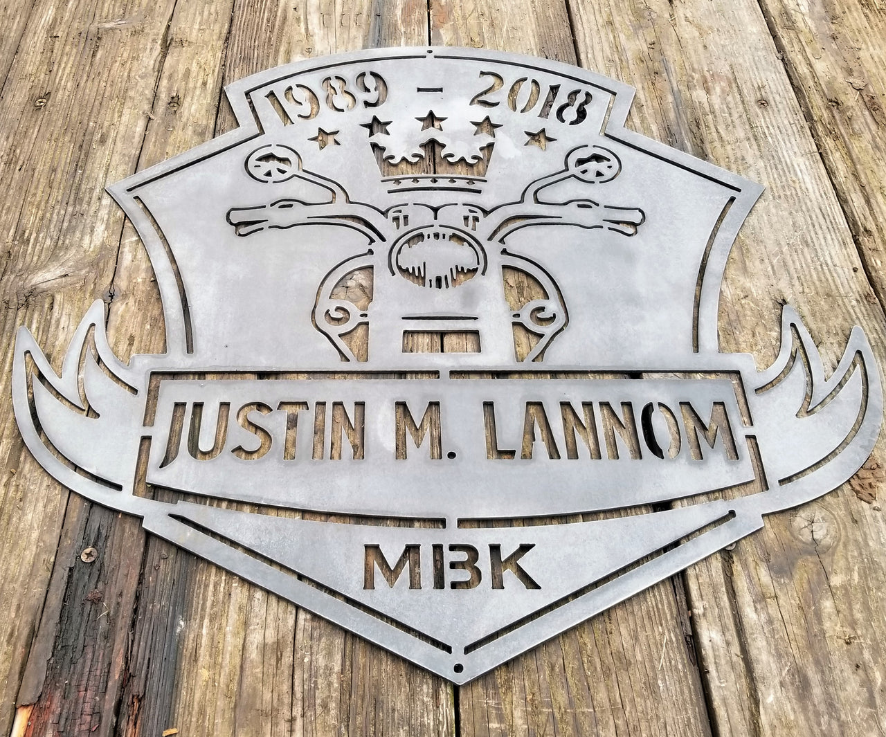 This is a memorial sign with an established year, dipicting an image of a motorcylce.  The bottom has a name and reads, "Justin M. Lannom".