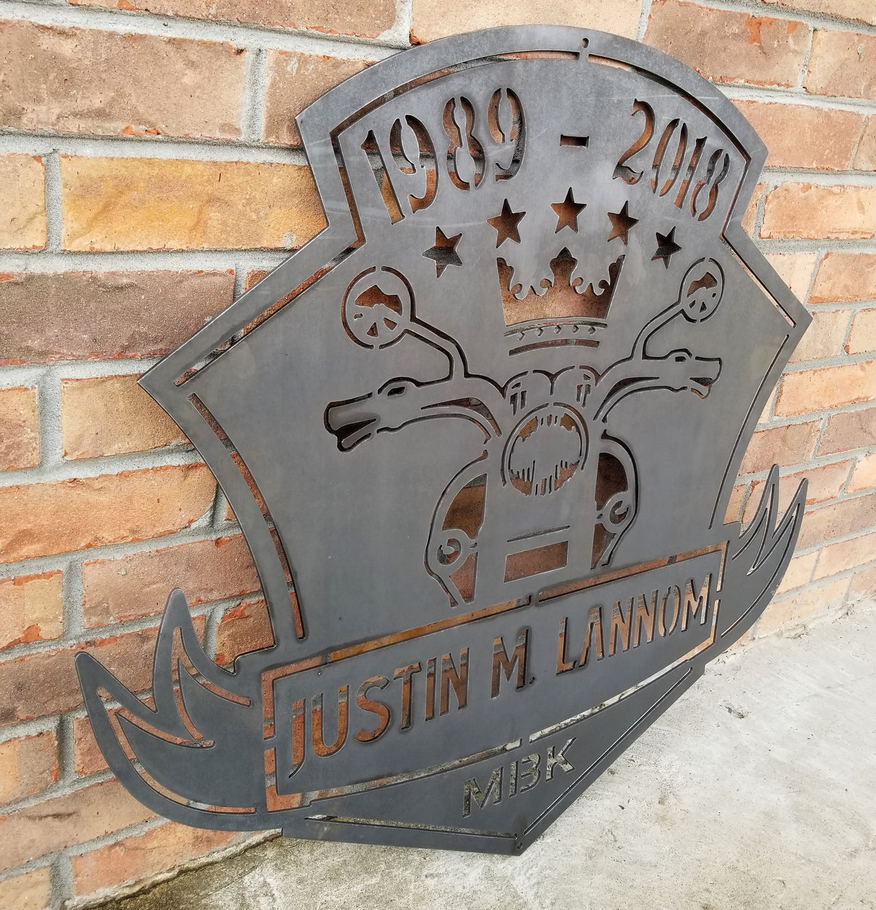 This is a memorial sign with an established year, dipicting an image of a motorcylce.  The bottom has a name and reads, "Justin M. Lannom".