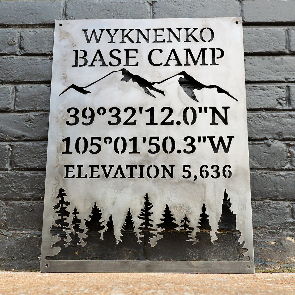 Rustic steel outdoor sign displaying latitude and longitude for cabin