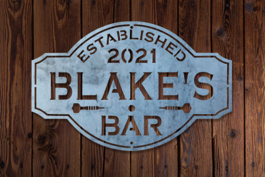 A vintage metal bar sign with the text 'ESTABLISHED 2021 BLAKE'S BAR' displayed on a wooden background.