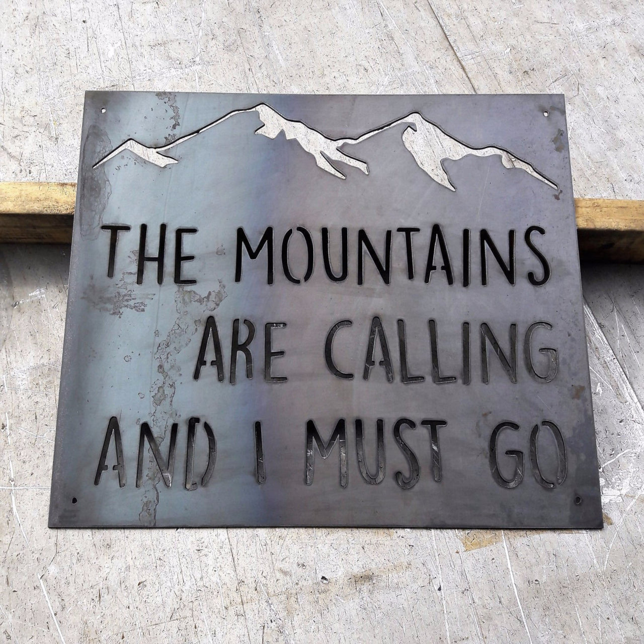 Custom metal  sign that is in the shape of a rectangle with the image of a mountain range at the top. The sign reads, "The Mountains are Calling and I Must Go"