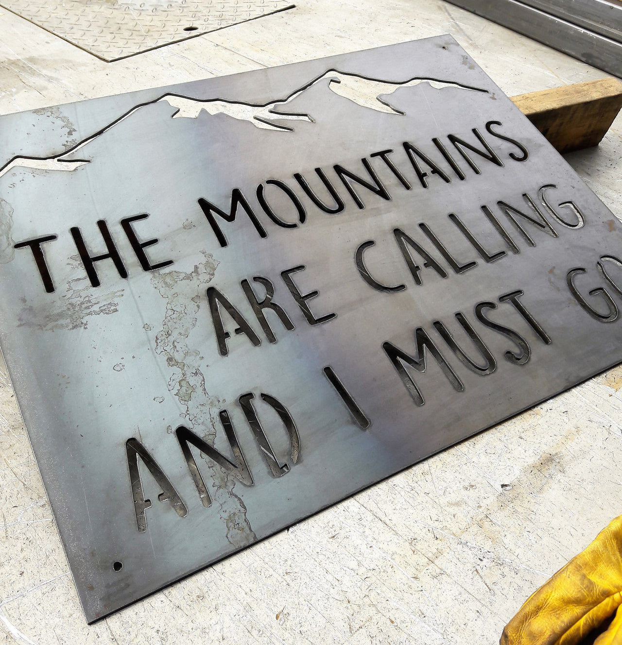Custom metal  sign that is in the shape of a rectangle with the image of a mountain range at the top. The sign reads, "The Mountains are Calling and I Must Go"