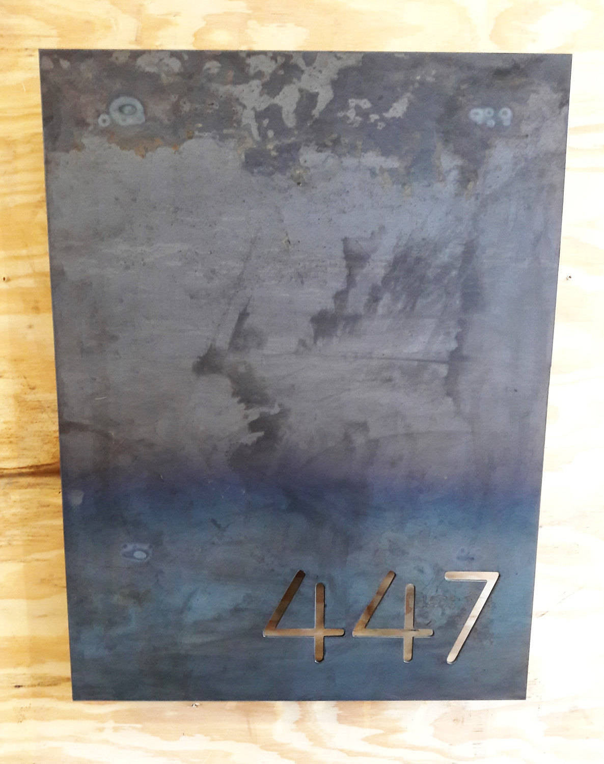 This is a personalized metal sign that has brackets welded to the back of the sign so that it stands one inch off the wall. It is a modern address sign in the shape of a rectangle and reads, "447"