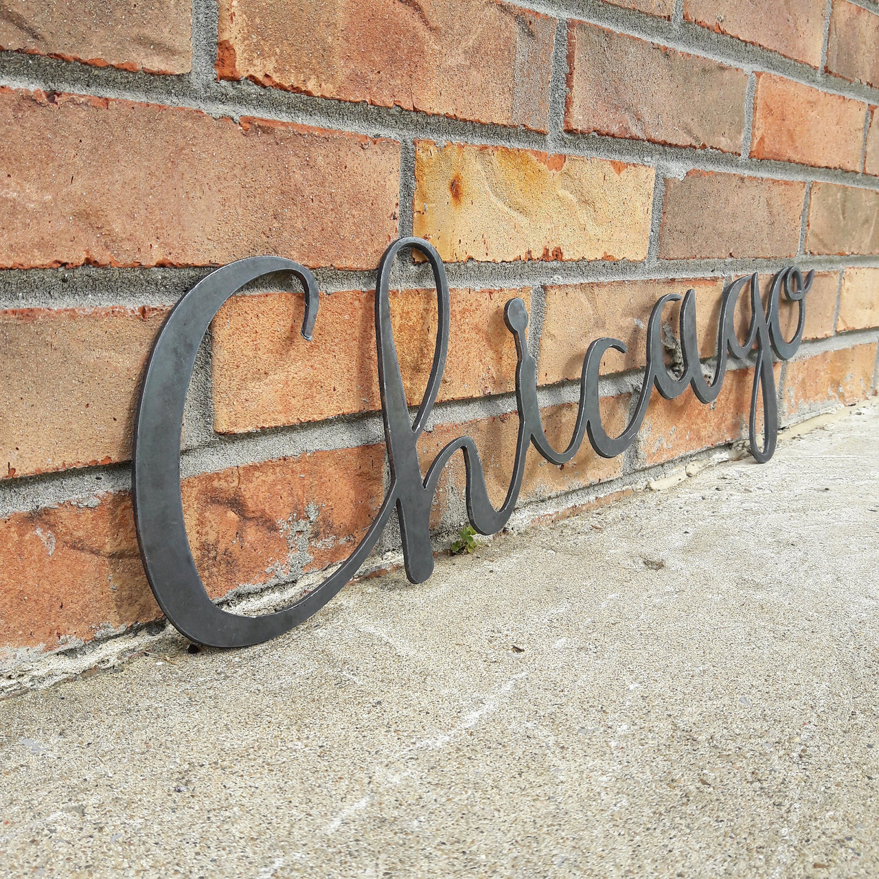 This metal home decor is in the shape of a cursive word and reads, "Chicago".