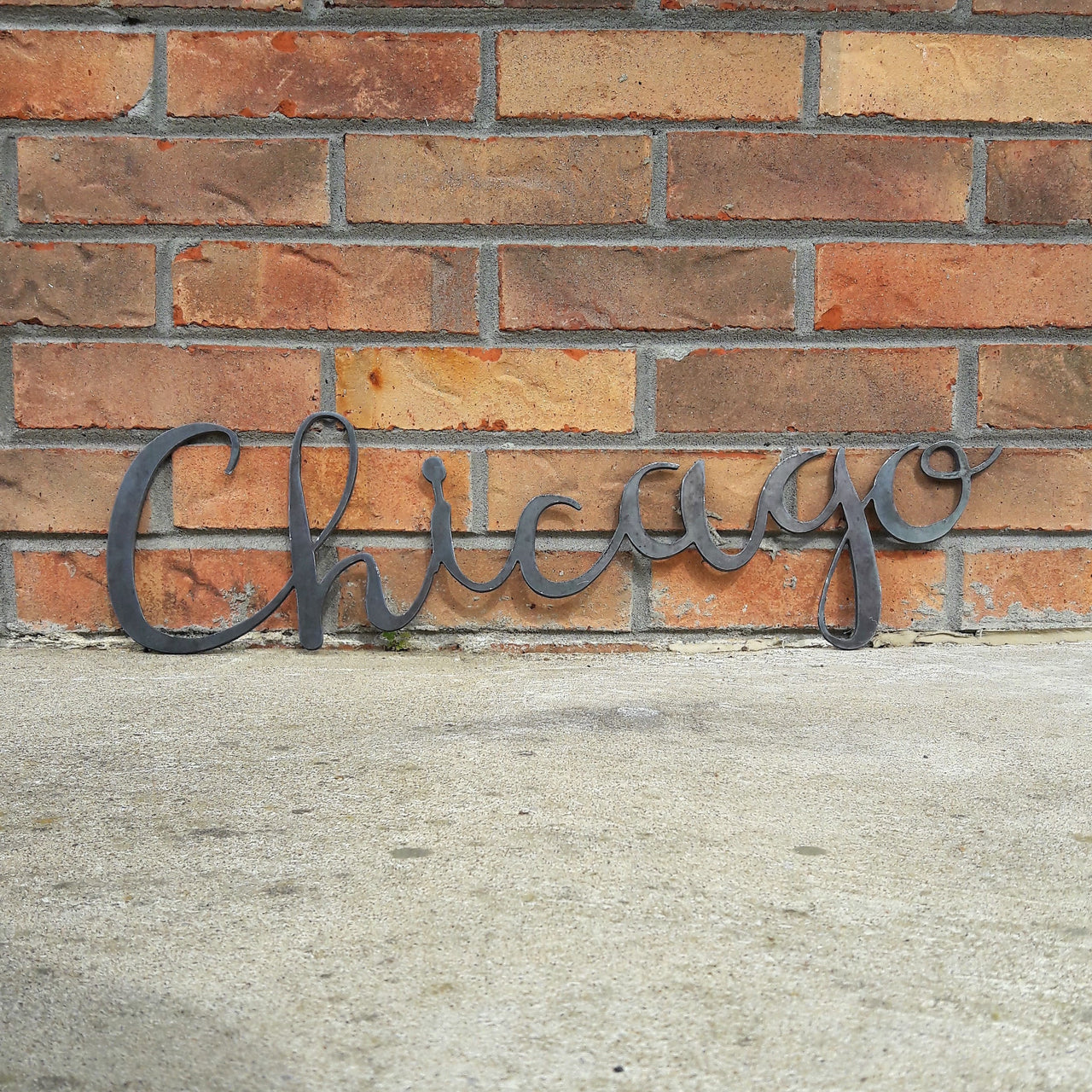 This metal home decor is in the shape of a cursive word and reads, "Chicago".