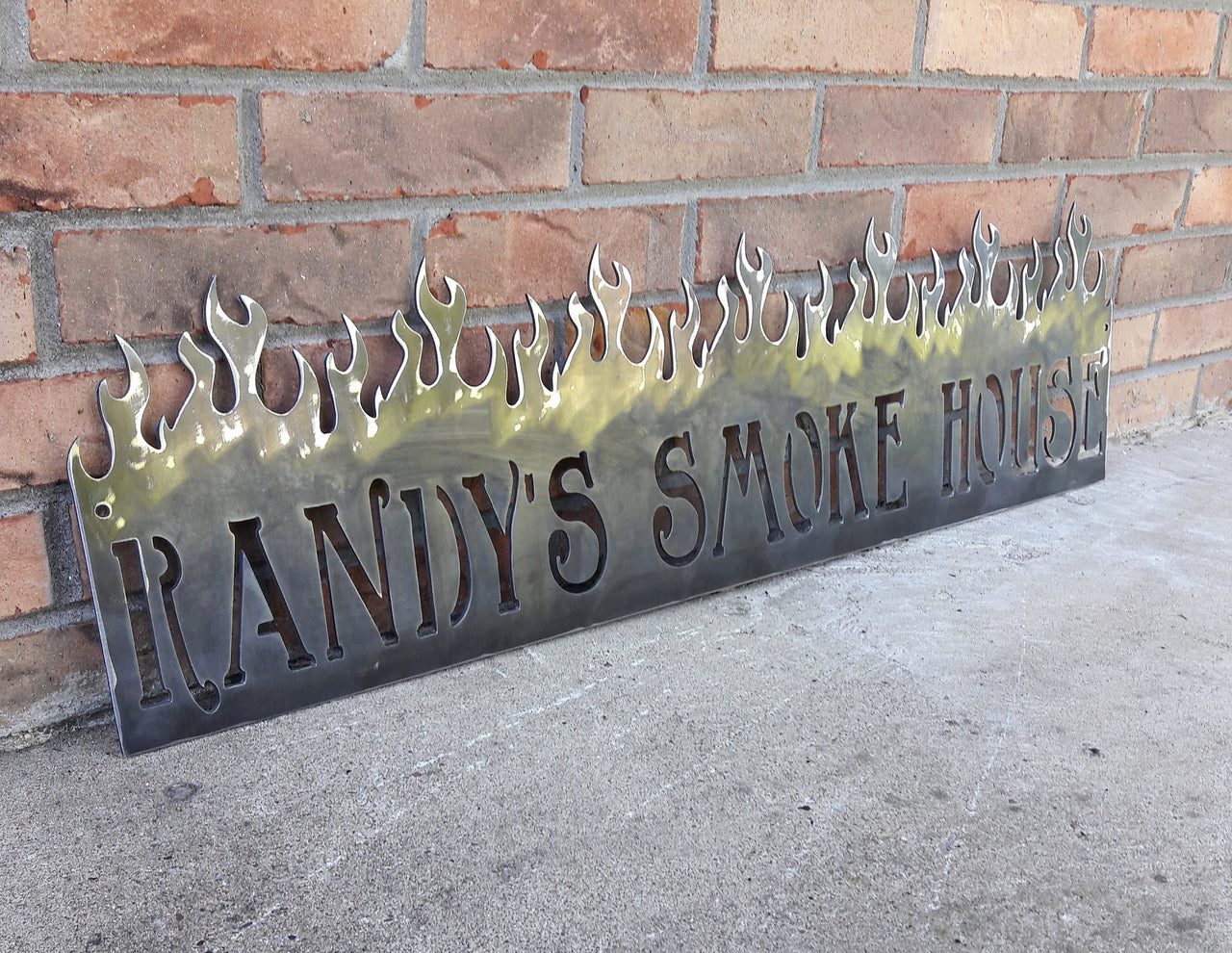 This is a personalized metal sign that features flames at the top and reads, " Randy's Smoke House".