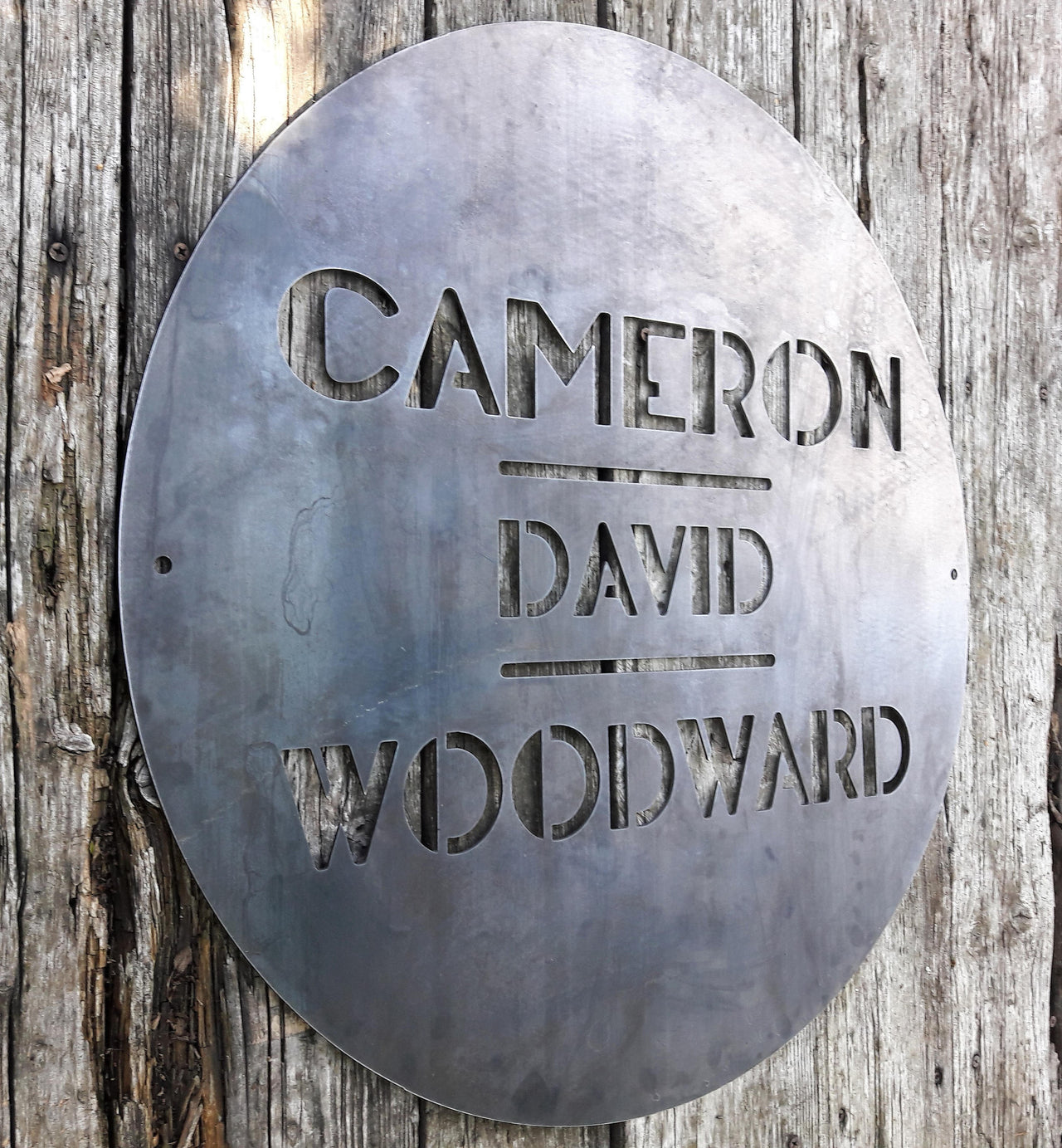 This is a round art deco sign that has three lines of text with a straight line seperating them. The sign reads, "Cameron David Woodward"