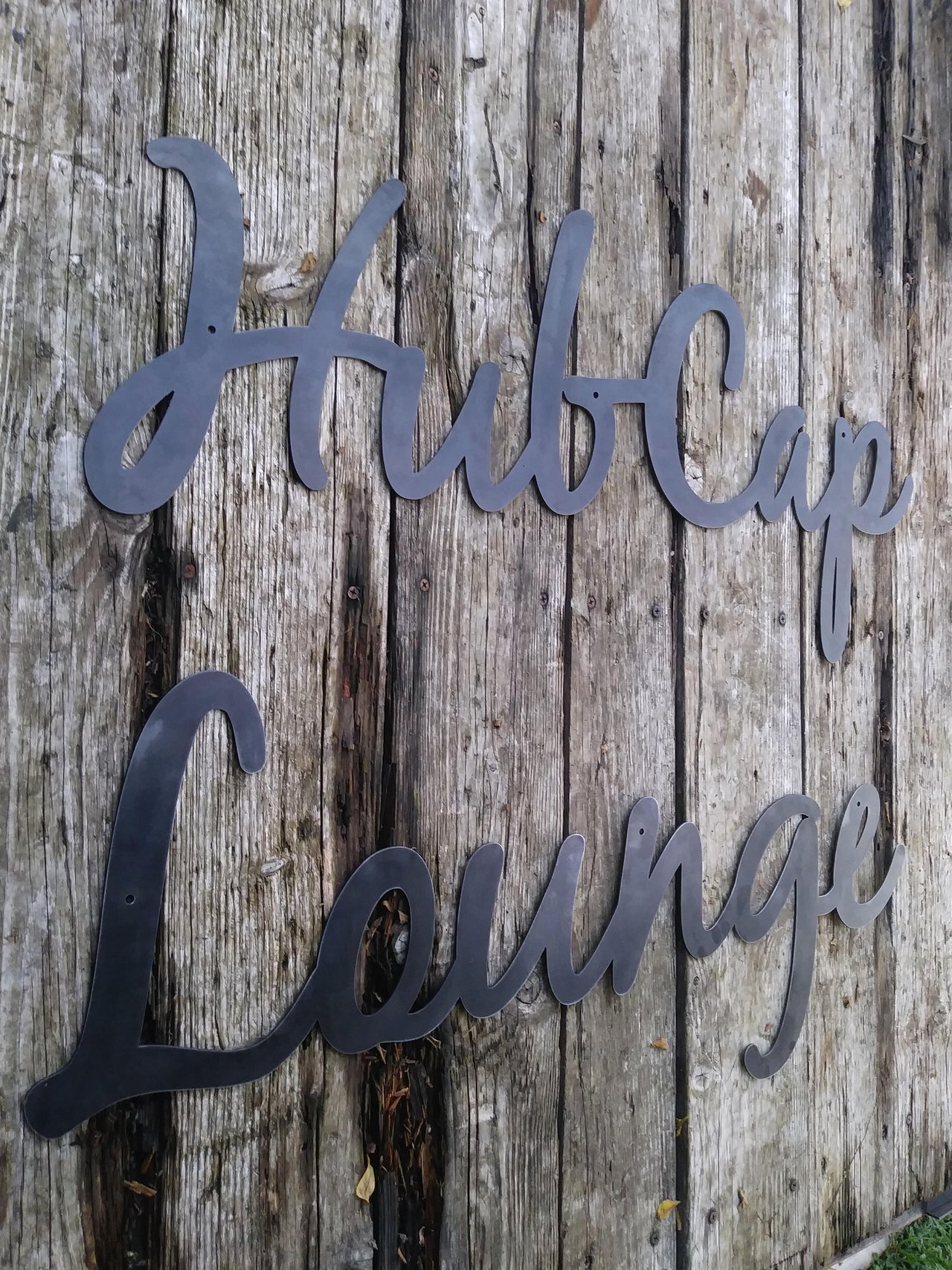 This is a custom metal cursive sign that is powder coated black and reads' "Hubcap Lounge".