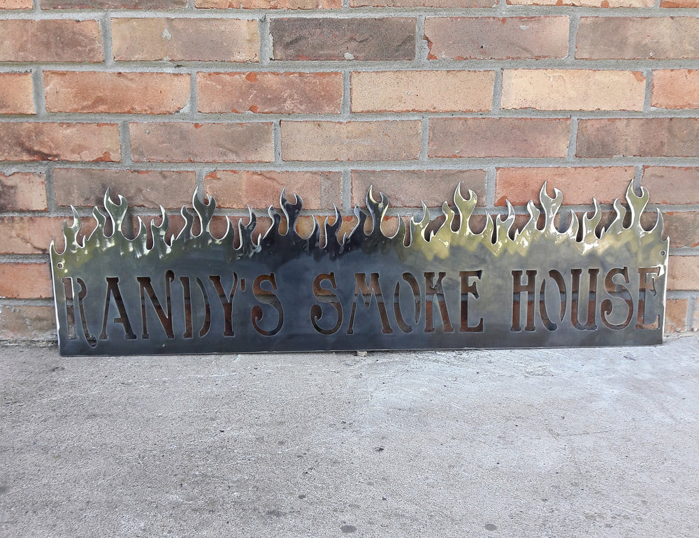 This is a personalized metal sign that features flames at the top and reads, " Randy's Smoke House".